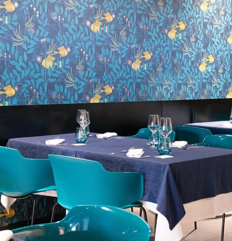 Apparecchiatura del tavolo del ristorante con sedie blu, tovaglia e carta da parati decorata.
