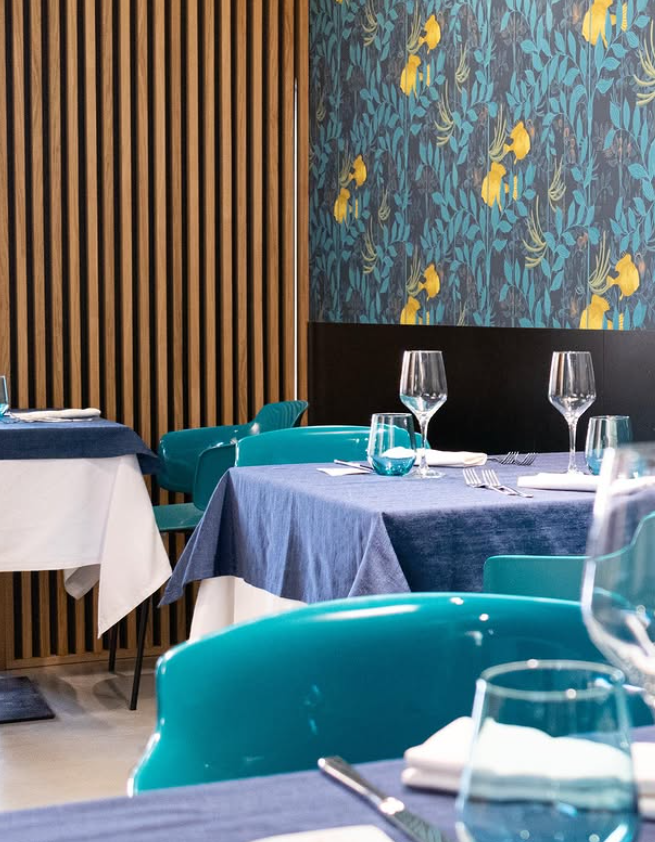 Sala da pranzo del ristorante con sedie color verde acqua, tovaglie blu e carta da parati floreale.