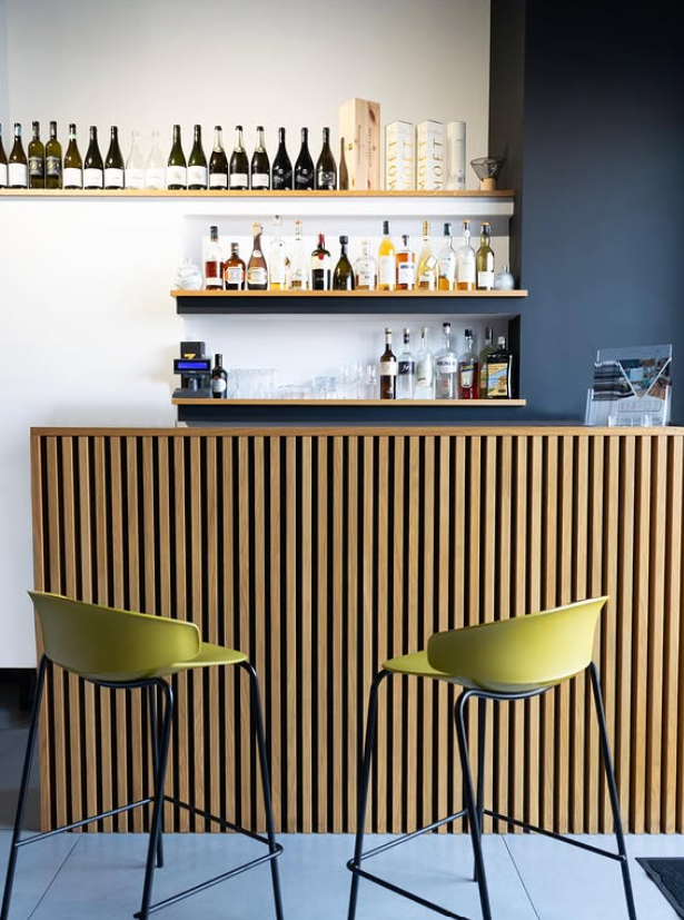 Bar con sgabelli verde oliva, facciata in legno e scaffali pieni di bottiglie.
