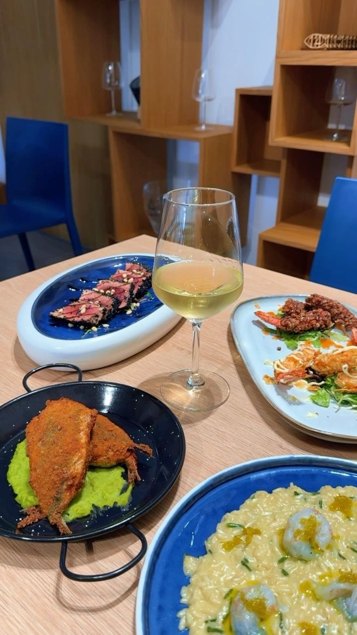 Un tavolo apparecchiato con piatti di cibo e un bicchiere di vino bianco in una moderna sala da pranzo.