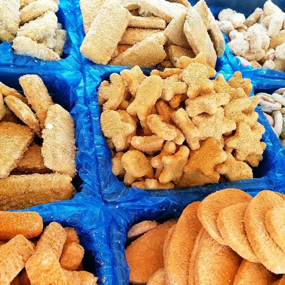 Assortimento di prodotti ittici surgelati e impanati, tra cui bastoncini e sagome di animali, in contenitori blu.