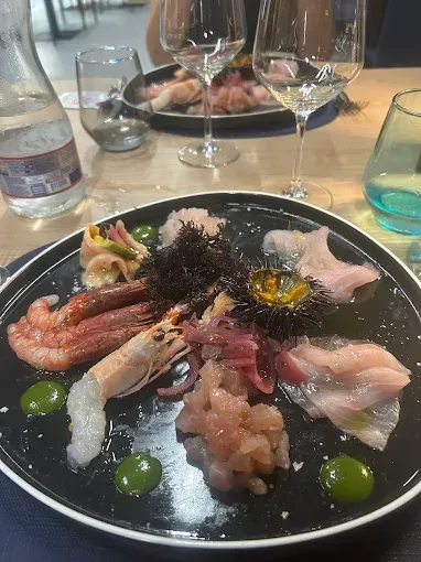 Piatto di frutti di mare con gamberi, pesce e contorni, con bicchieri da vino e bottiglia d'acqua su un tavolo.