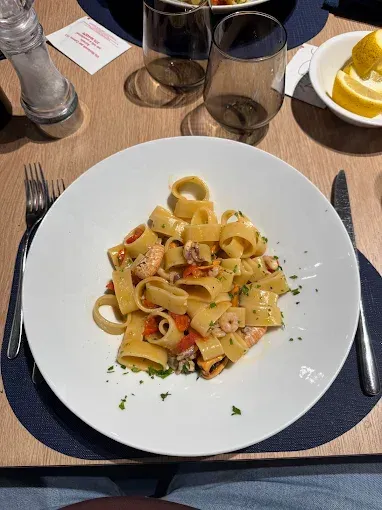 Piatto di pasta con frutti di mare su un piatto bianco, servito su un tavolo con posate e bevande.