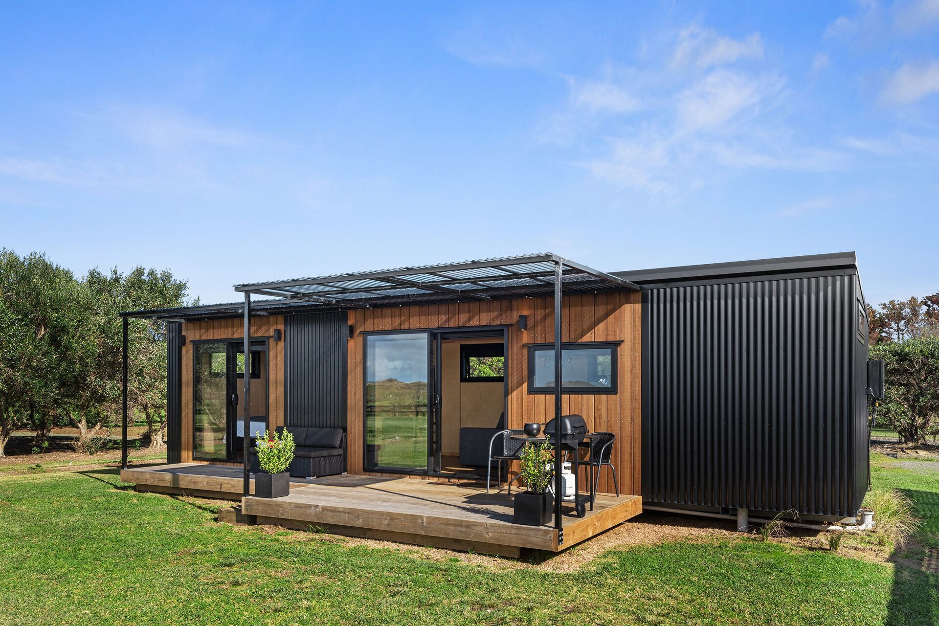 Modern cabin with wooden facade, black accents, and small patio on a green lawn.