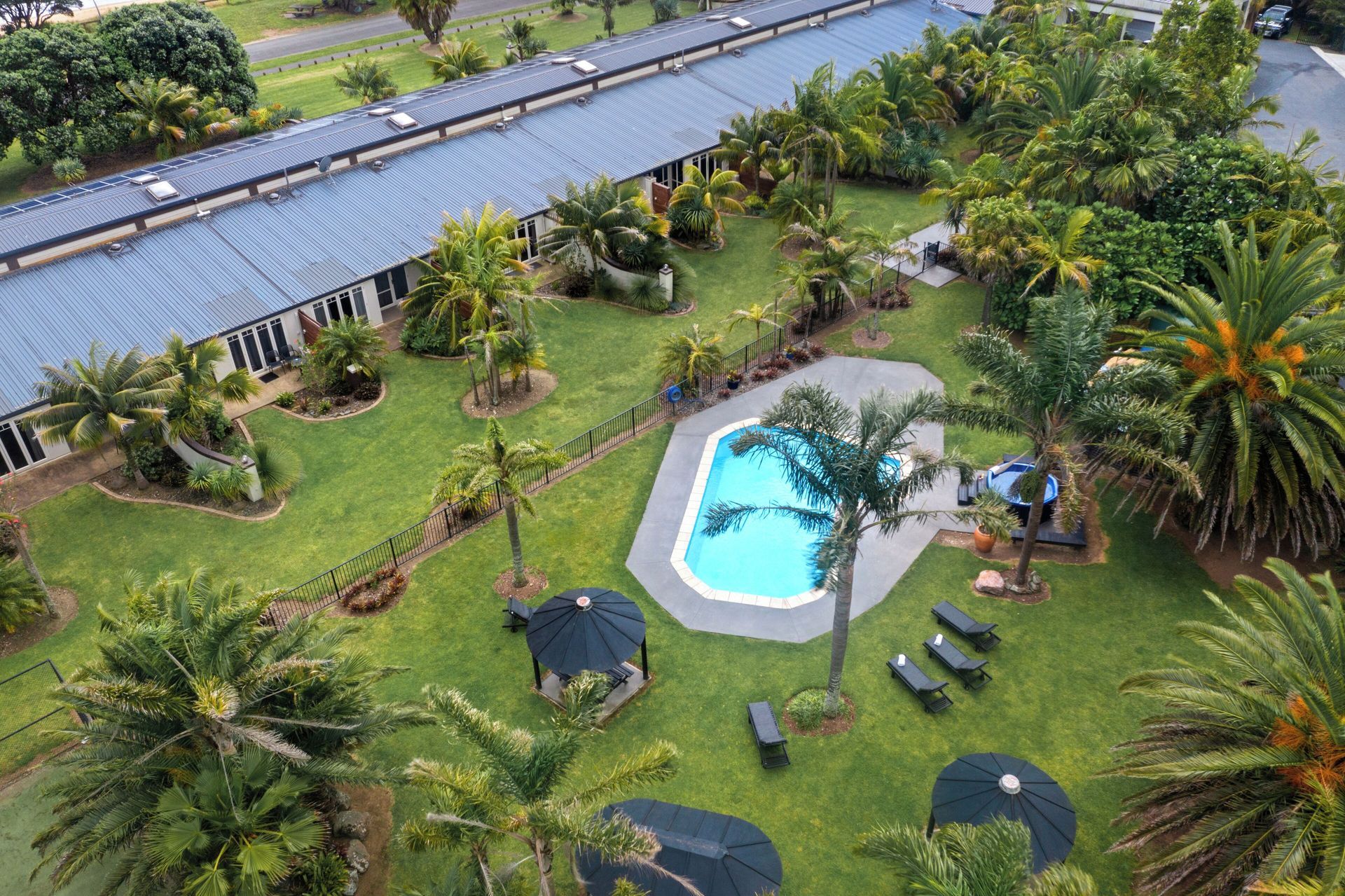 Aerial view of a resort with a pool, palm trees, and a long building.