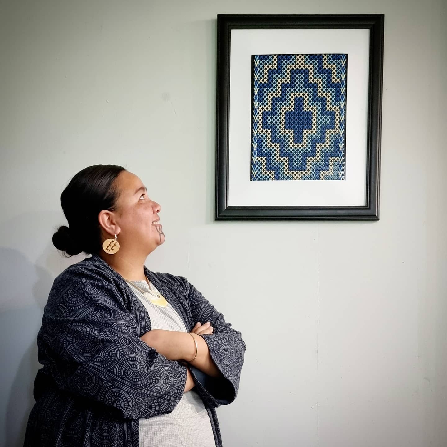 A woman is standing in front of a framed picture on a wall.