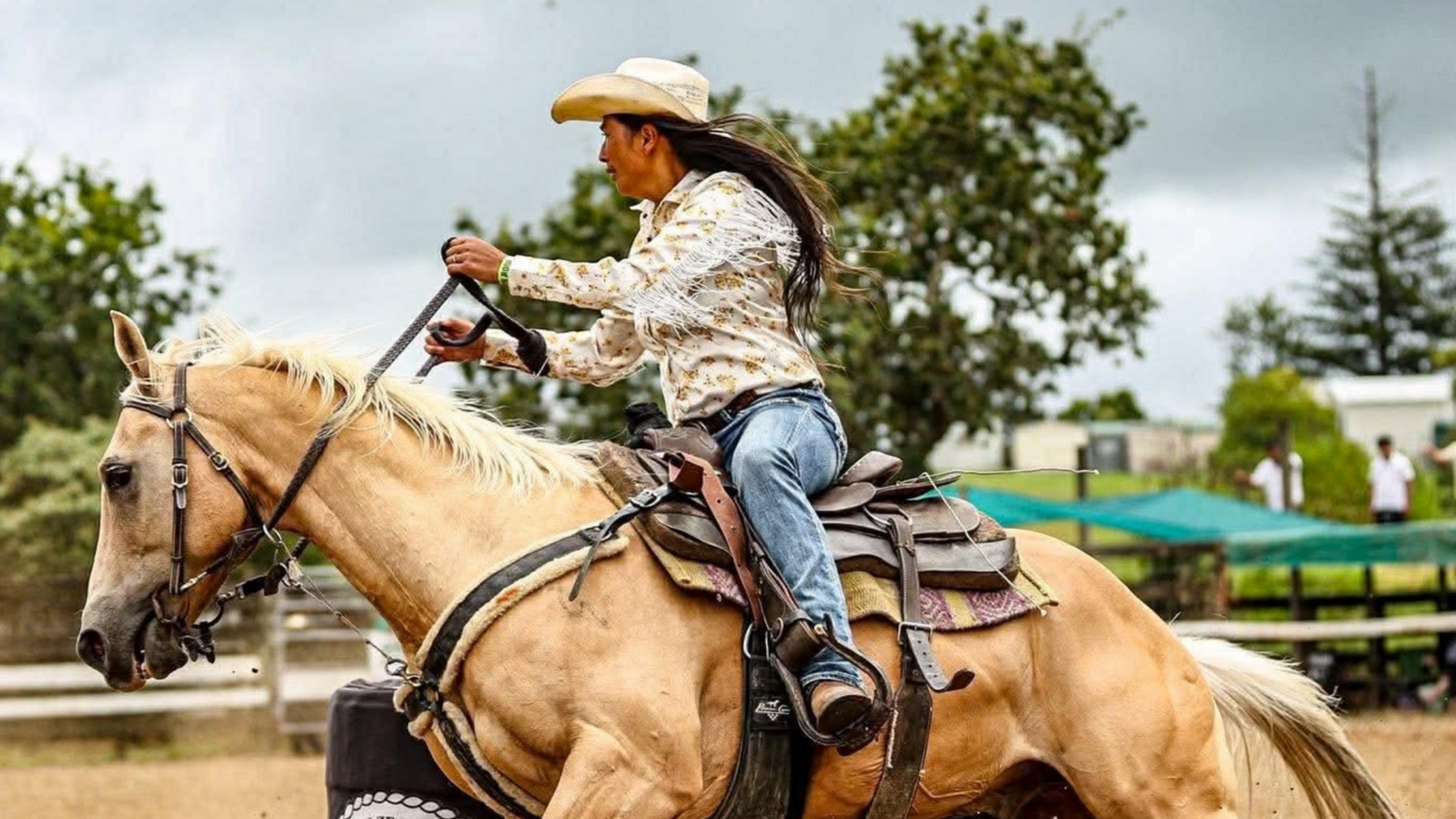 A rider on a palomino horse rounds a barrel during a competition.