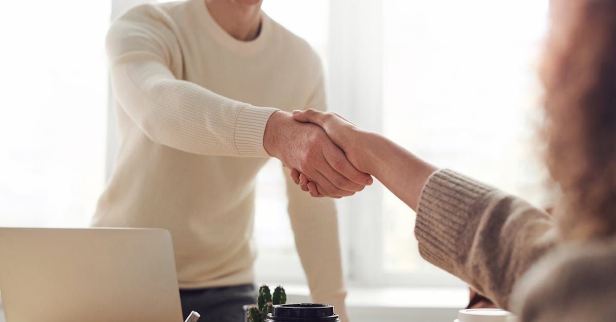 A man and a woman are shaking hands in front of a laptop.
