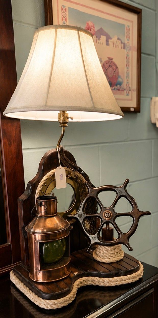 Vintage table lamp with cream shade, brass base, and nautical wheel decor on a woven tray