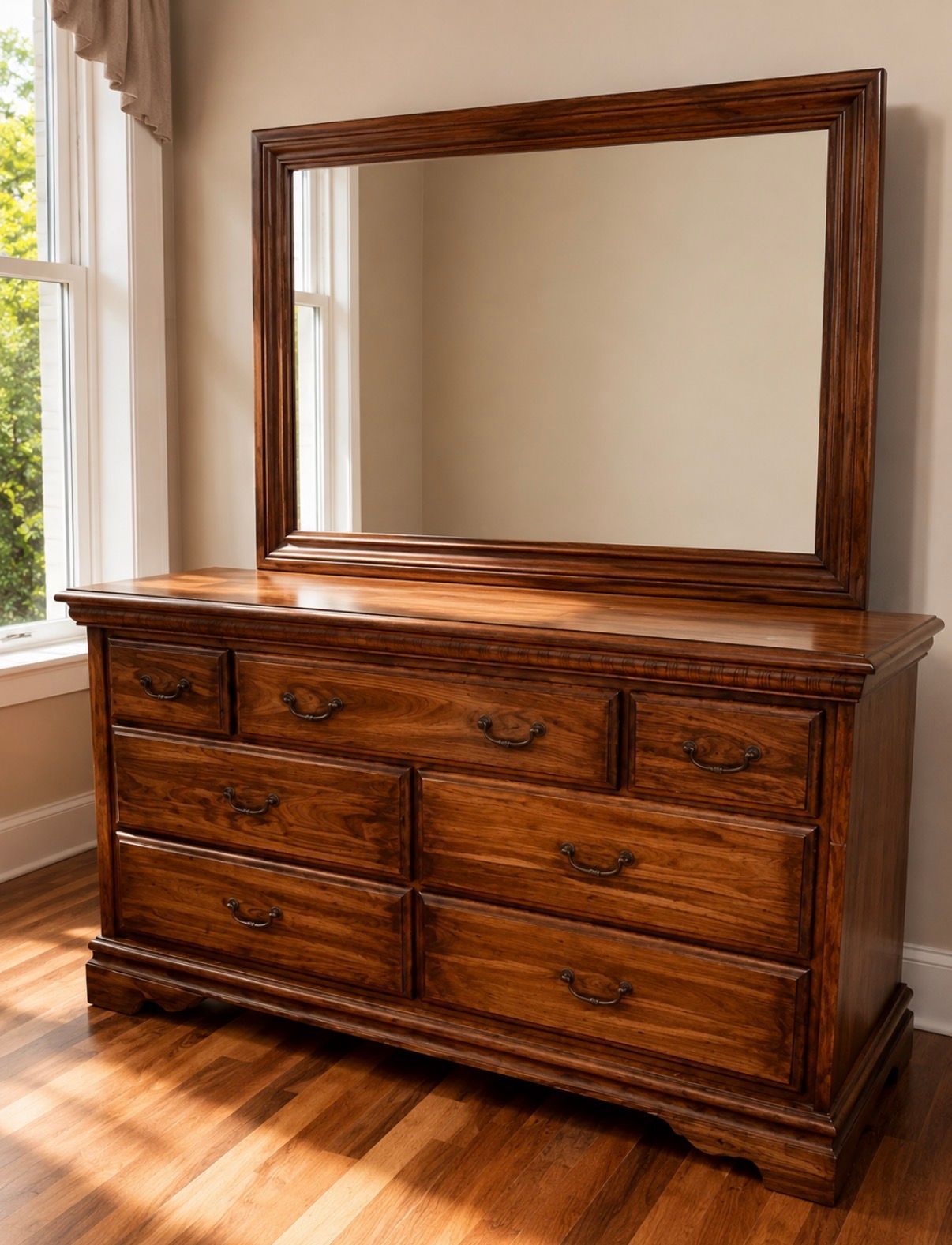 Wooden dresser with a large framed mirror in a sunlit room by a window