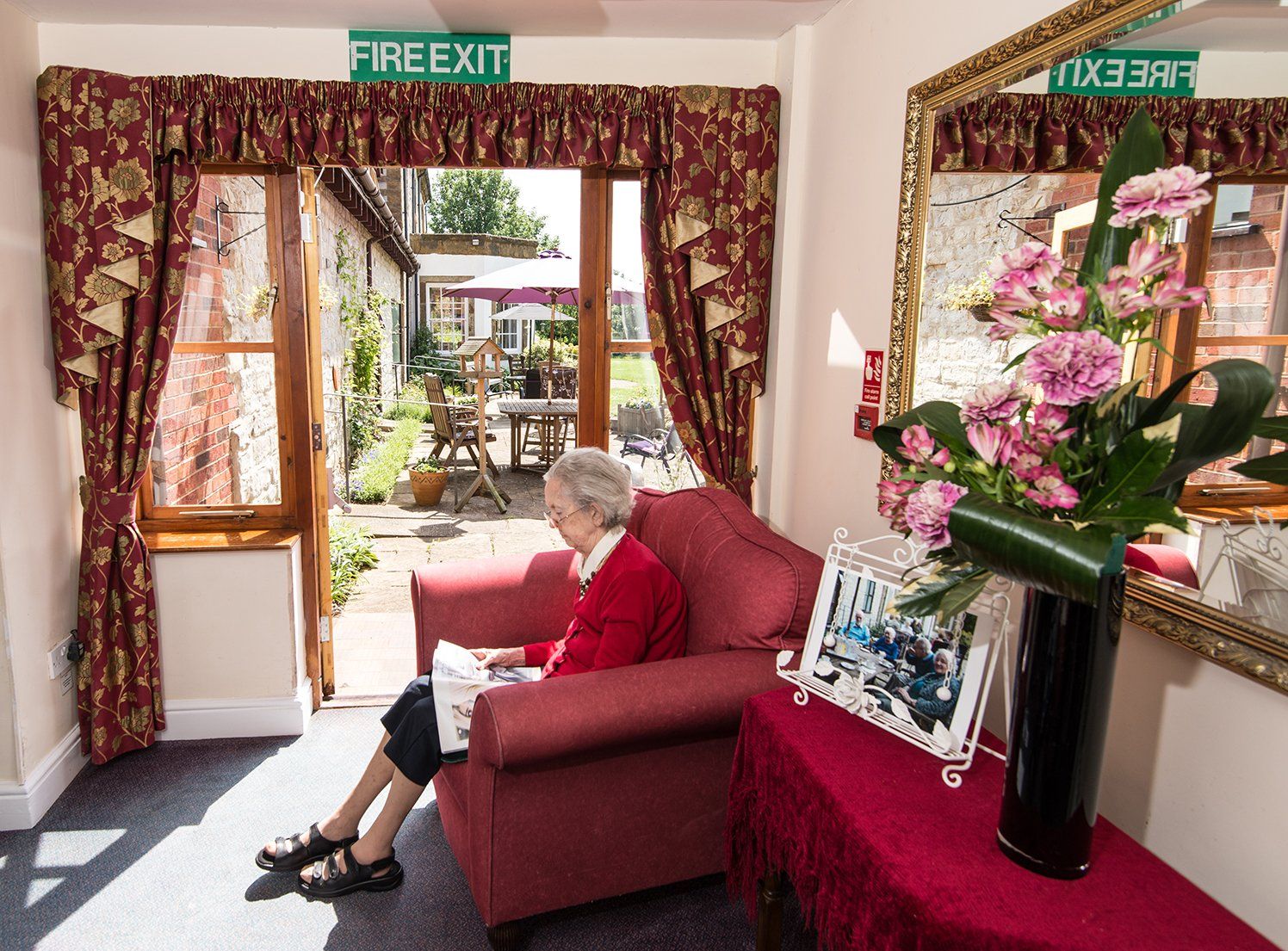 a lady sitting in a red sofa and reading a newspaper