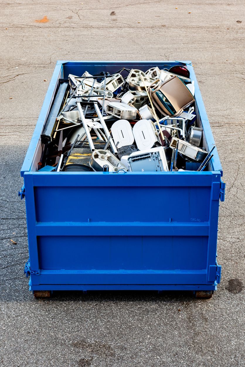 Blue dumpster overflowing with scrap metal on concrete surface.