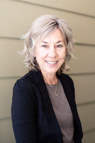 Woman with short blonde hair in a black outfit, sitting in a chair outdoors.