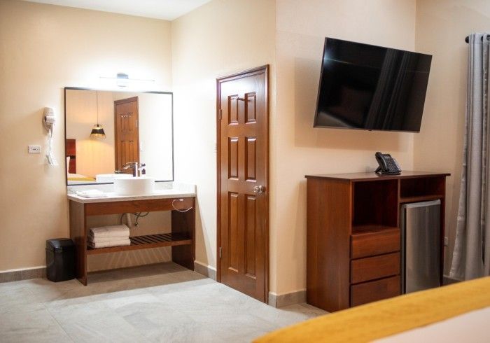 A hotel room with a bed , television , sink and mirror.