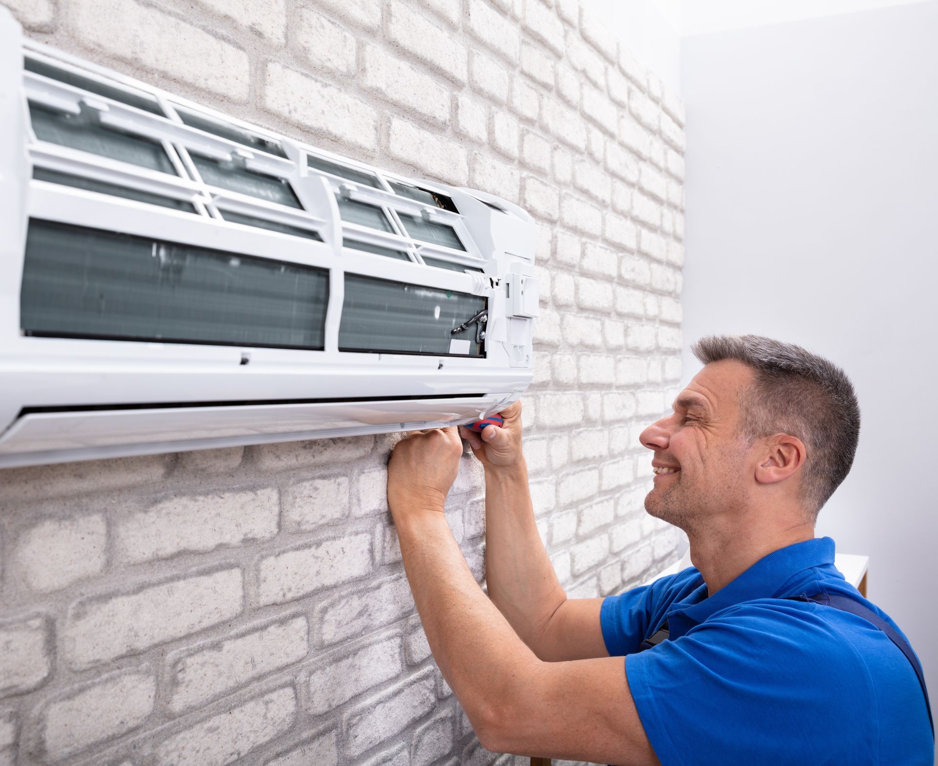 A technician is repairing a wall-mounted air conditioner unit using tools