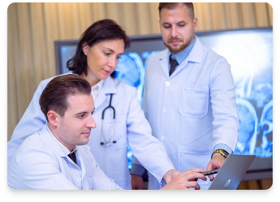 Tres médicos revisan una computadora portátil, en un entorno hospitalario, mirando una exploración cerebral.