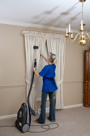 A woman is cleaning curtains with a vacuum cleaner.