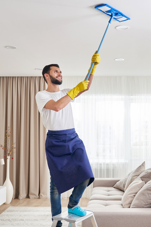 A man is standing on a ladder cleaning the ceiling with a mop.