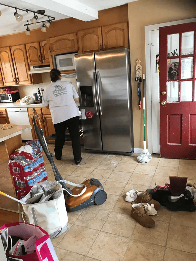 A woman is cleaning a kitchen with a vacuum cleaner.