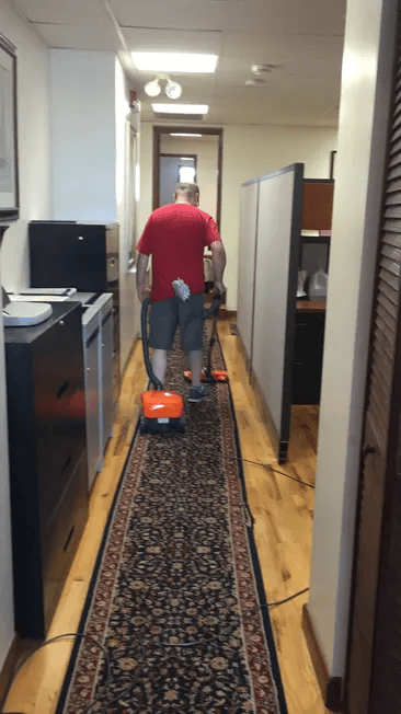 A man in a red shirt is vacuuming a long hallway