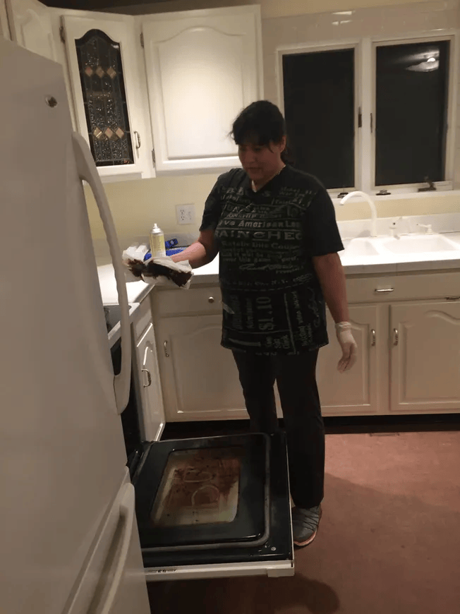 A woman in a black shirt is standing in a kitchen looking into an oven.