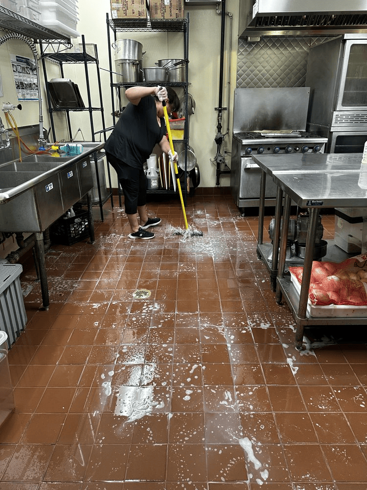 A woman is cleaning the floor of a kitchen with a mop.