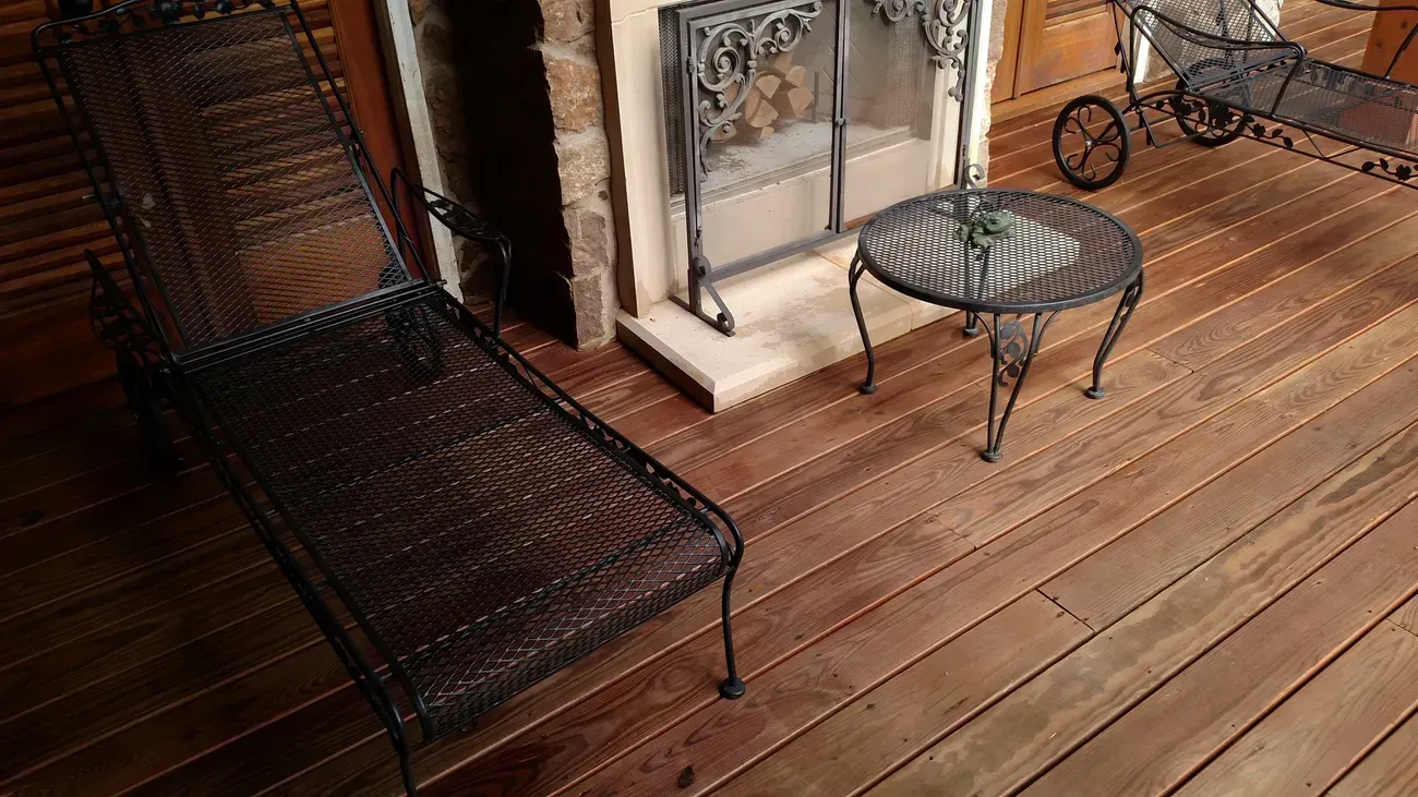 Wrought iron lounge chair and table on a wooden deck next to a fireplace.