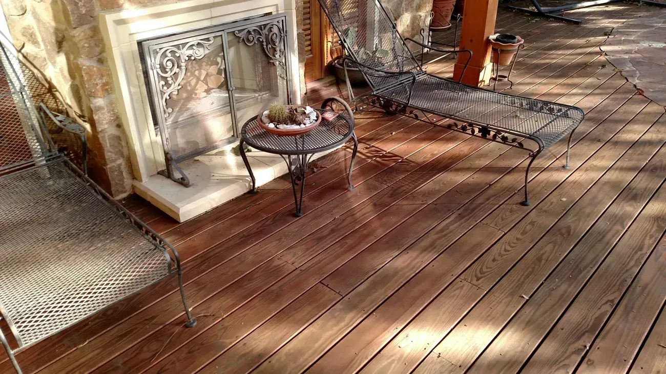 Outdoor deck with a fireplace, metal furniture, and a small table with items.