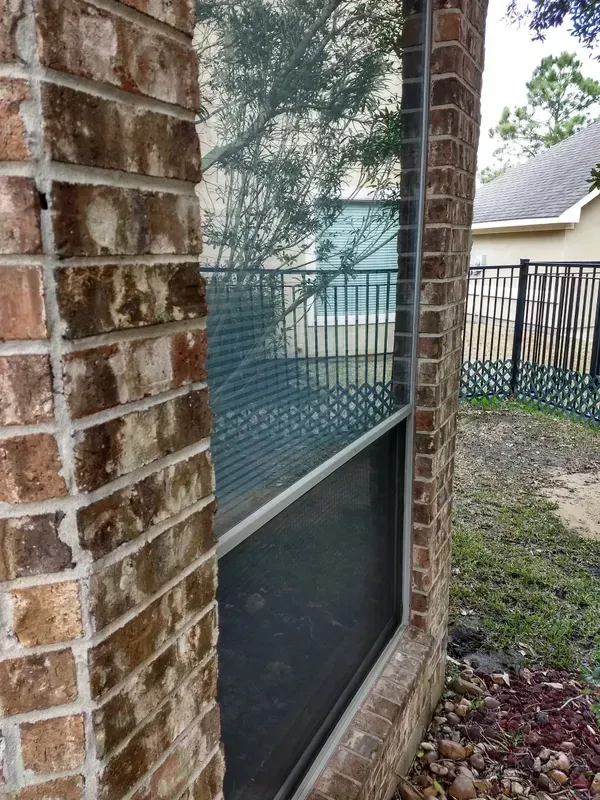 Window framed by brick, reflecting a fence and trees.