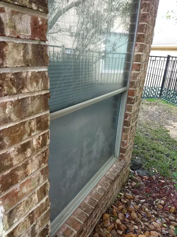 Brick building with a window. The window reflects a blurry outdoor scene.