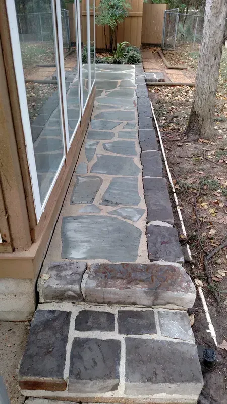 Stone walkway alongside a building with large windows and a small retaining wall.