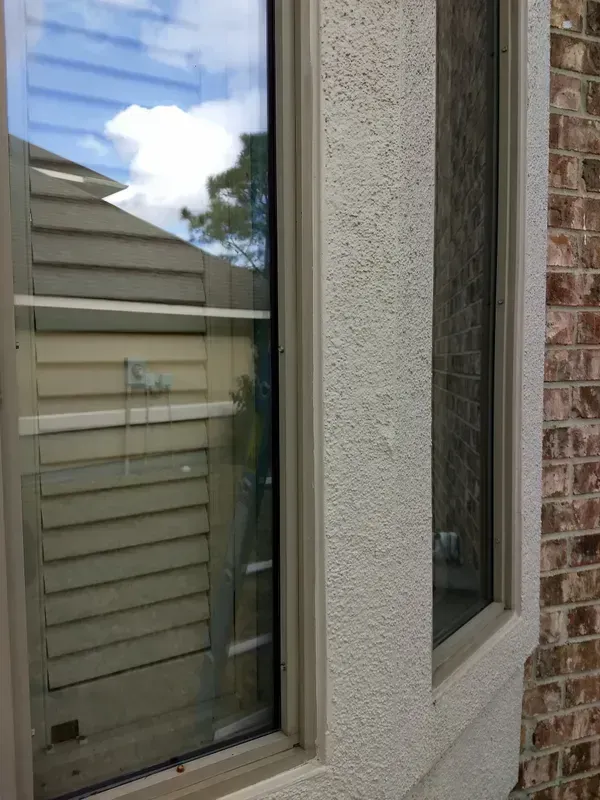 Exterior view of a window with white stucco and brick, reflecting a cloudy sky and wooden siding.