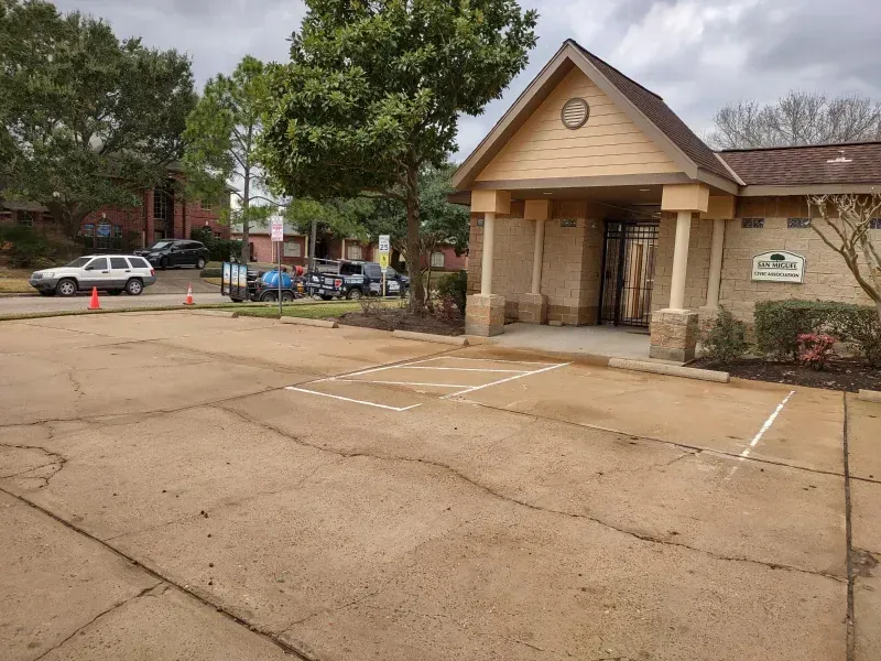 Exterior view of a building with a parking lot. A few vehicles and some trees are in the background.