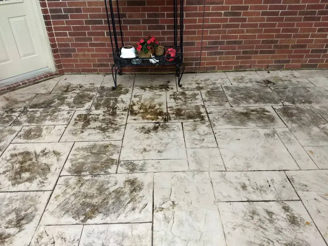 Stamped concrete patio with dark stains near a brick wall and a decorative shelf.