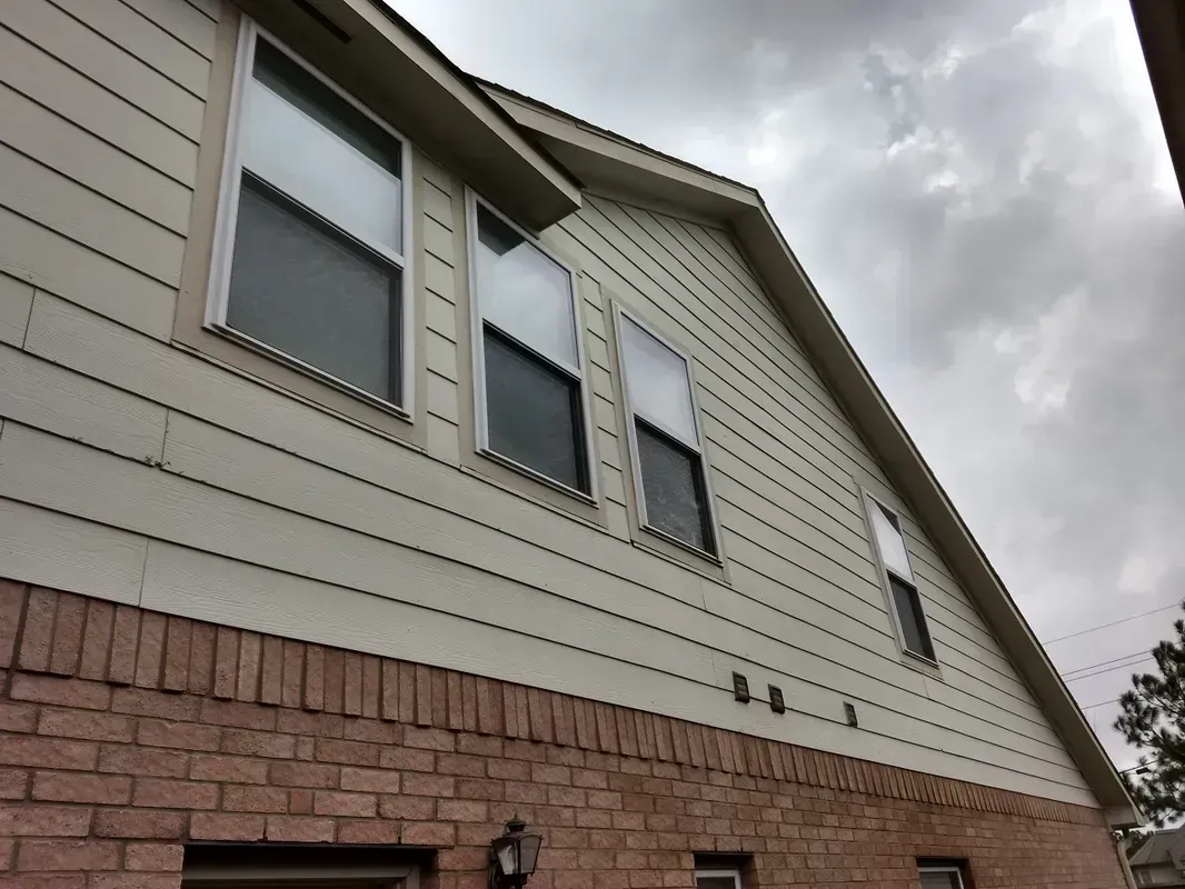 Brick and beige siding house with multiple windows against a cloudy sky.