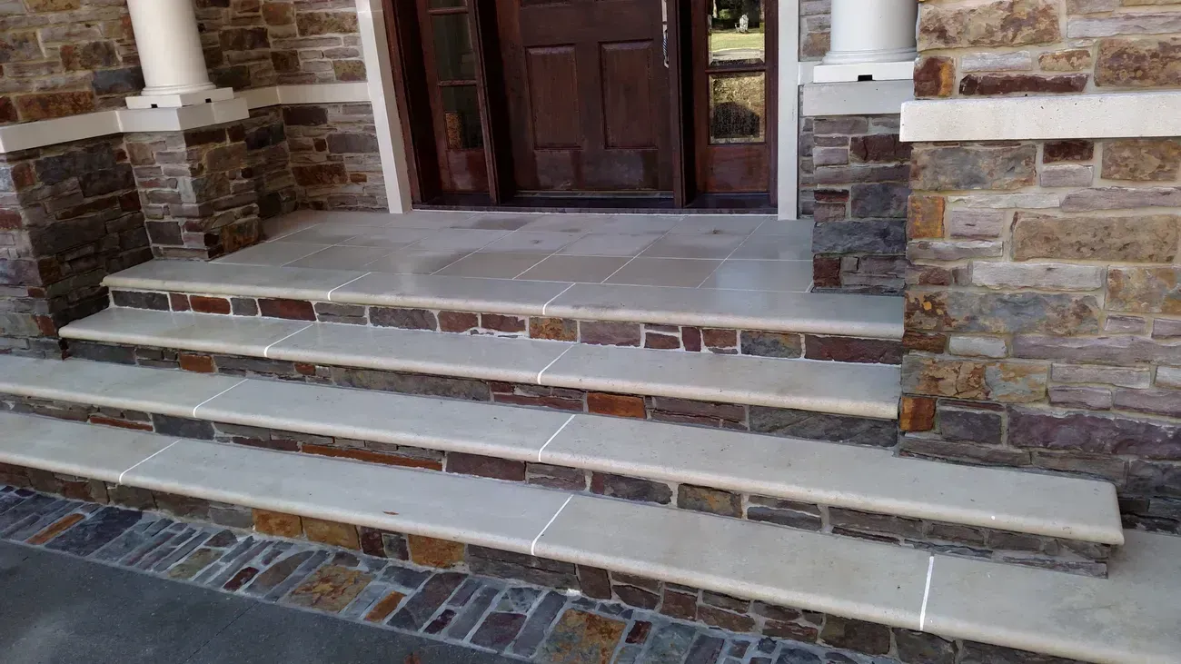 Stone steps leading to a wooden door. The steps are light stone with dark stone and brick accents.