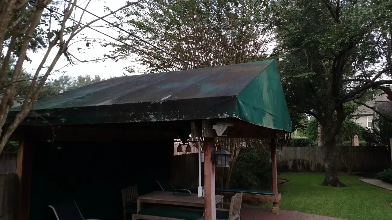 Green-roofed gazebo on a wooden deck in a backyard with green grass and trees.