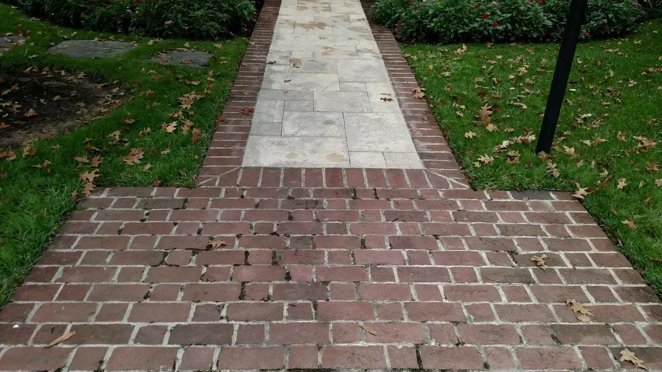 Brick pathway leads to stone walkway through grassy lawn.
