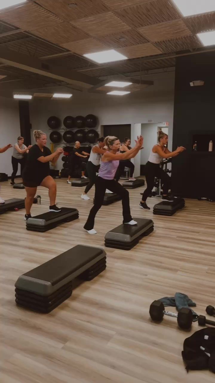 Pilates studio with wooden floor, mirrors, exercise machines, and white curtains. Ceiling has exposed beams.
