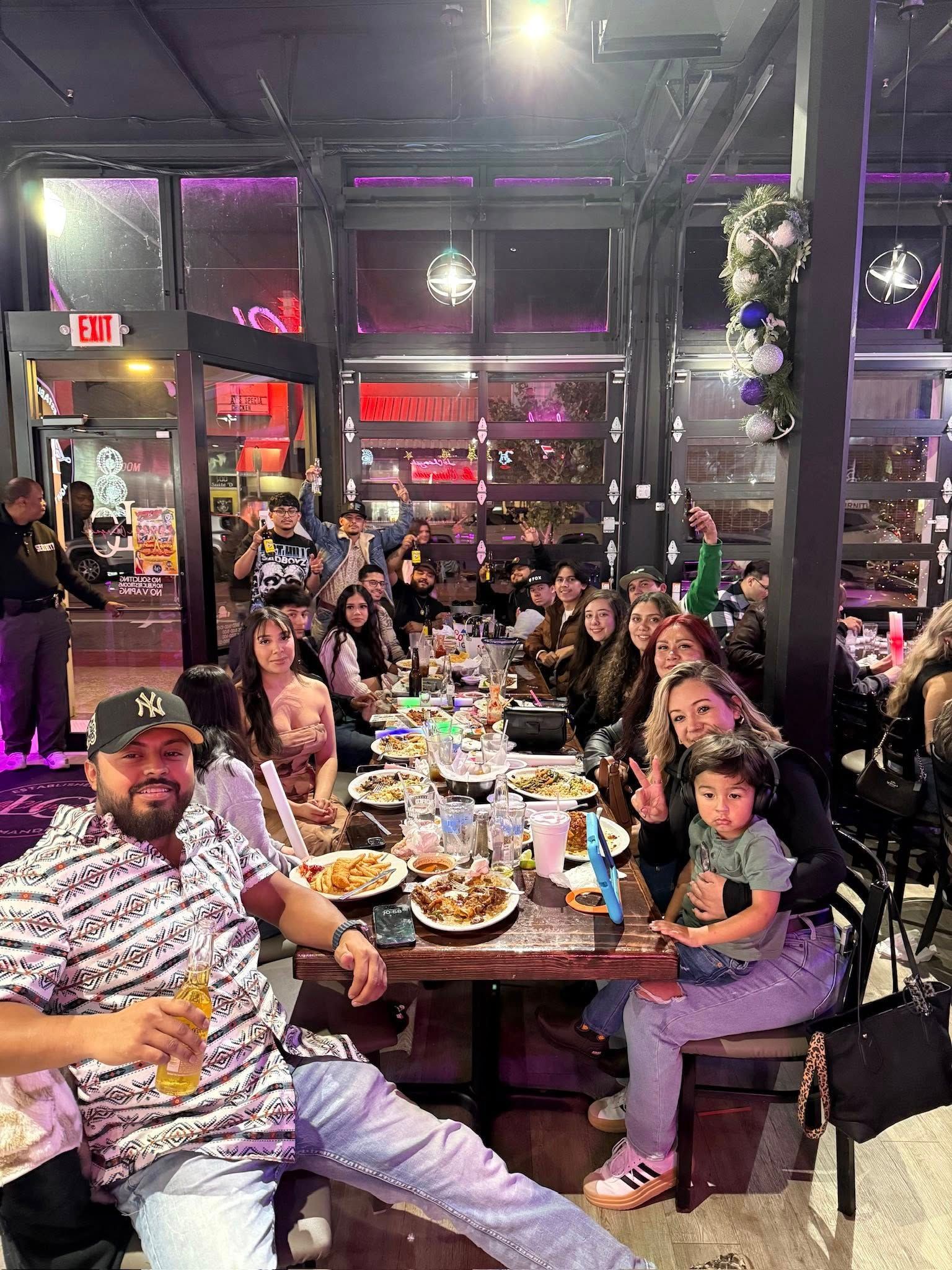 Large group dining at a restaurant, seated around a crowded table with plates, drinks, and smiling faces. Large group dining at a restaurant, seated around a crowded table with plates, drinks, and smiling faces.