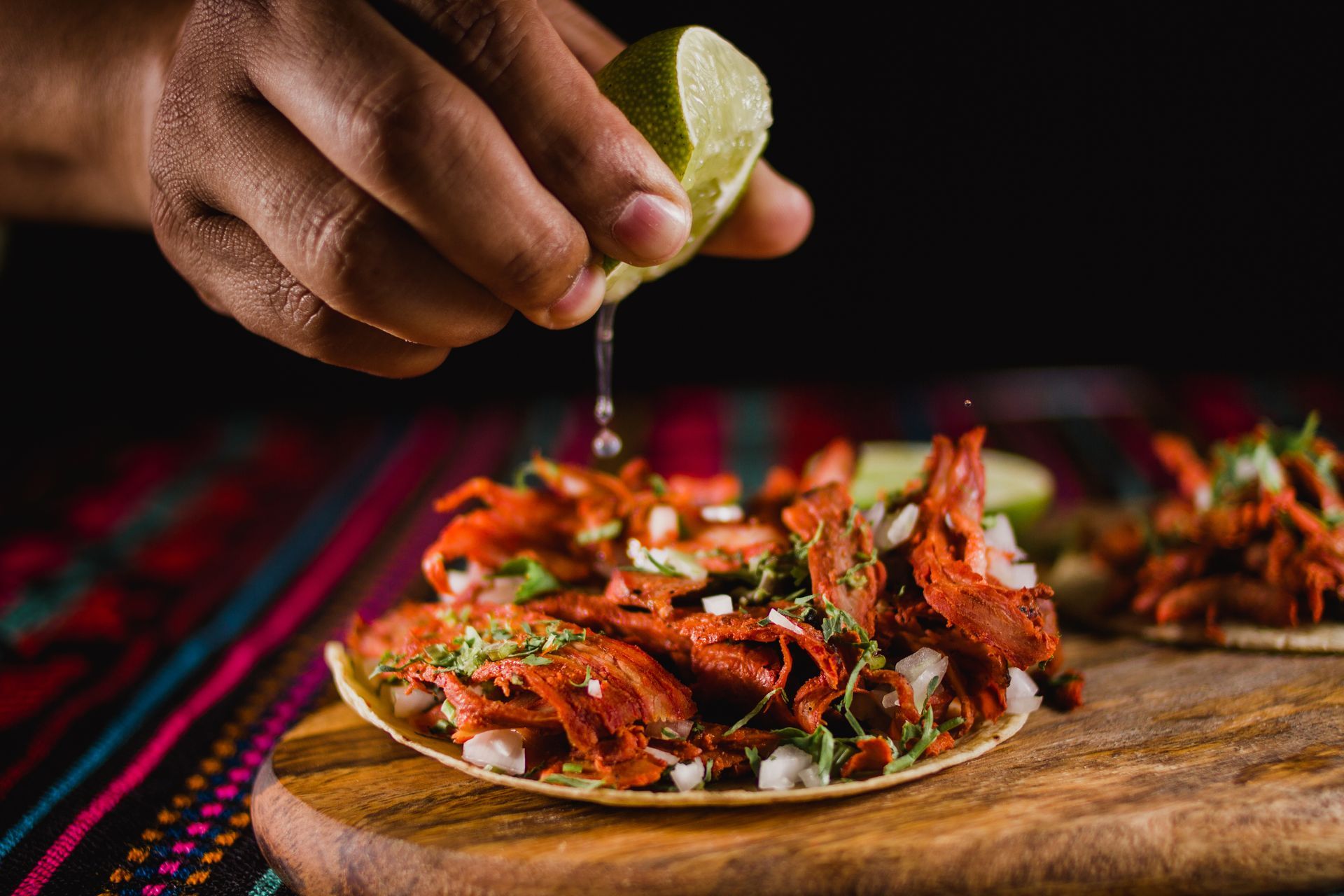 Hand squeezing lime over a plate of spicy fried food on a wooden board