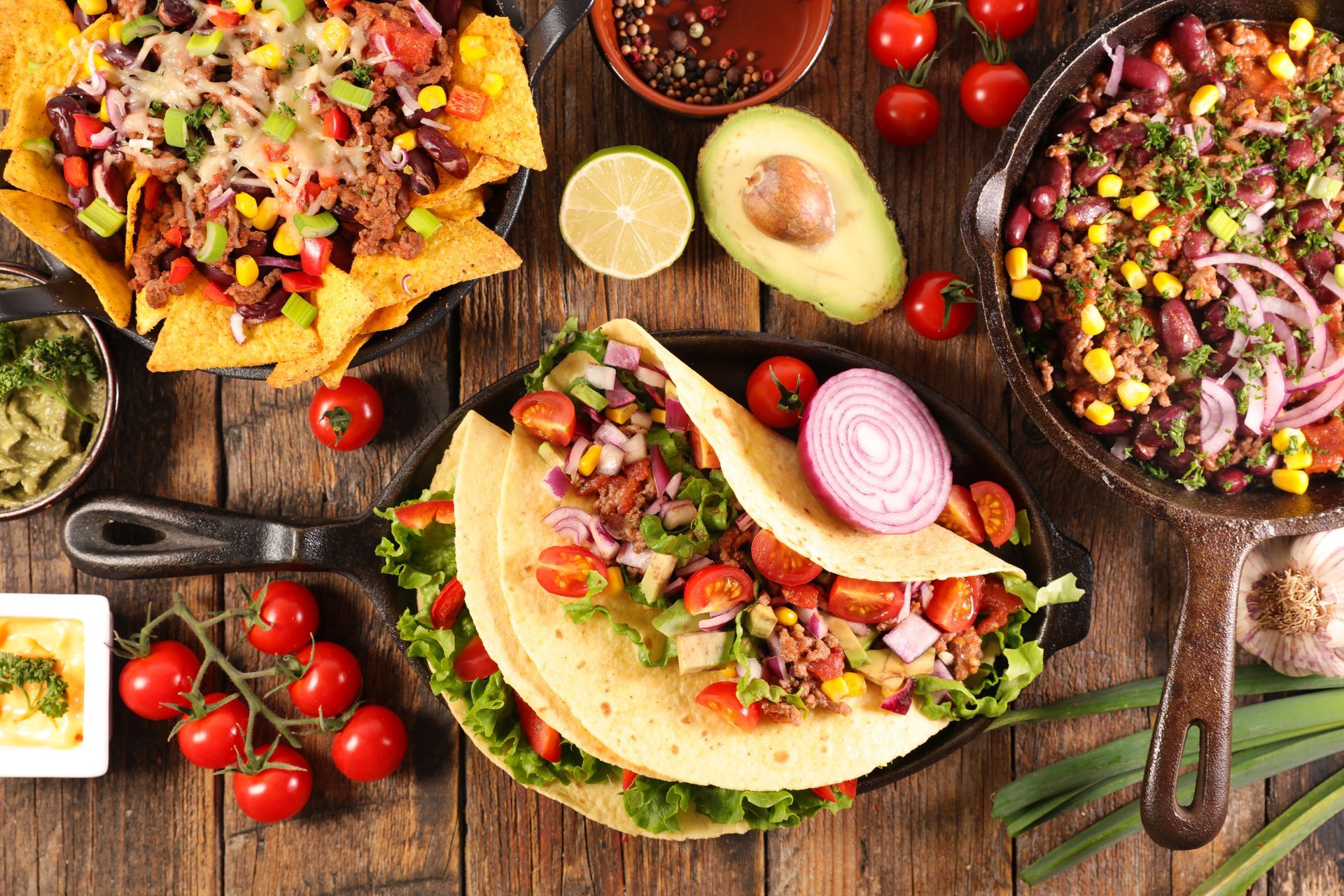 Three colorful tacos topped with vegetables on a rustic wooden table with avocados and salsa Three colorful tacos topped with vegetables on a rustic wooden table with avocados and salsa
