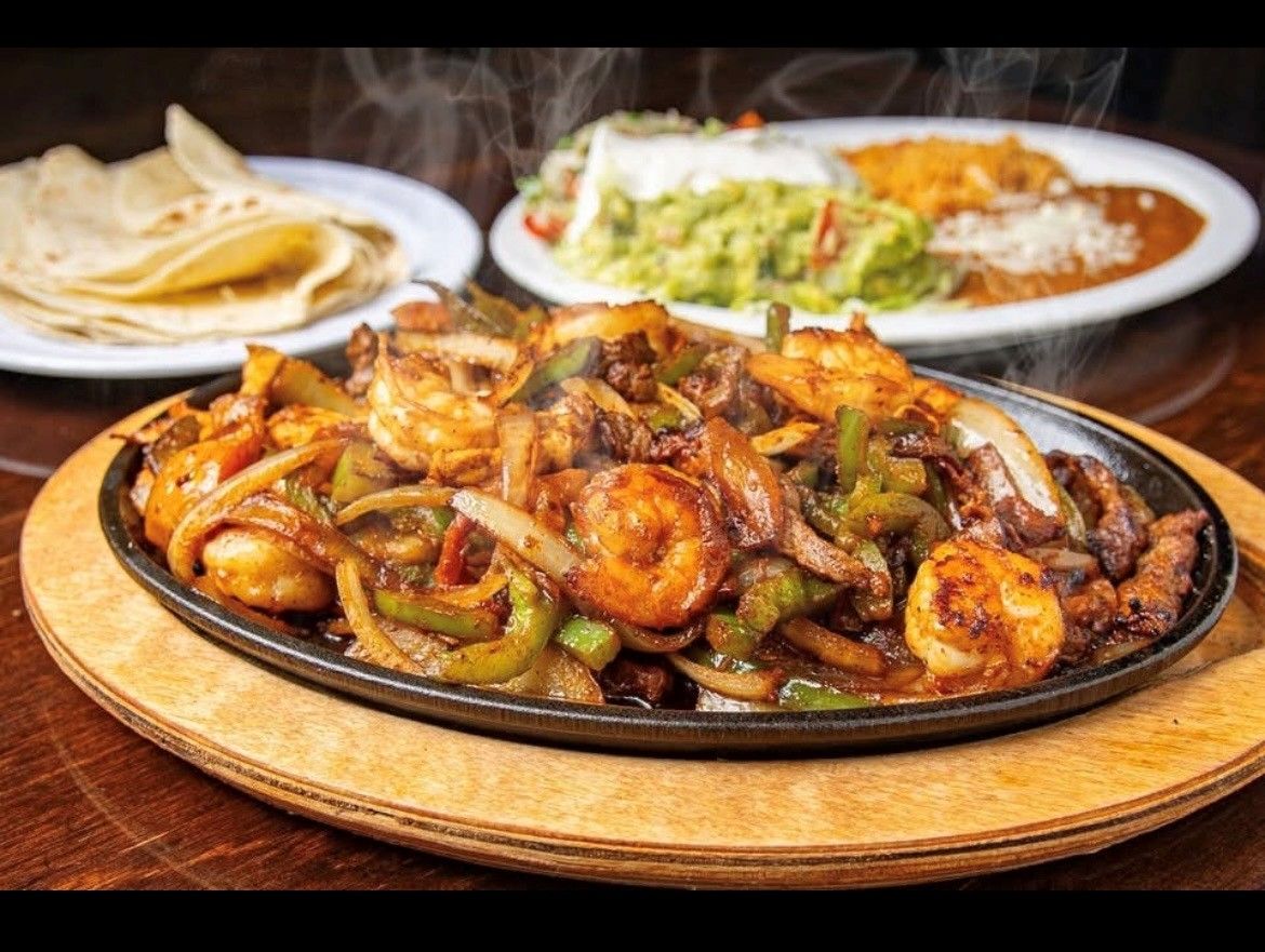 Three plates of colorful tacos and tortilla chips on a black table with lime wedges and sauces