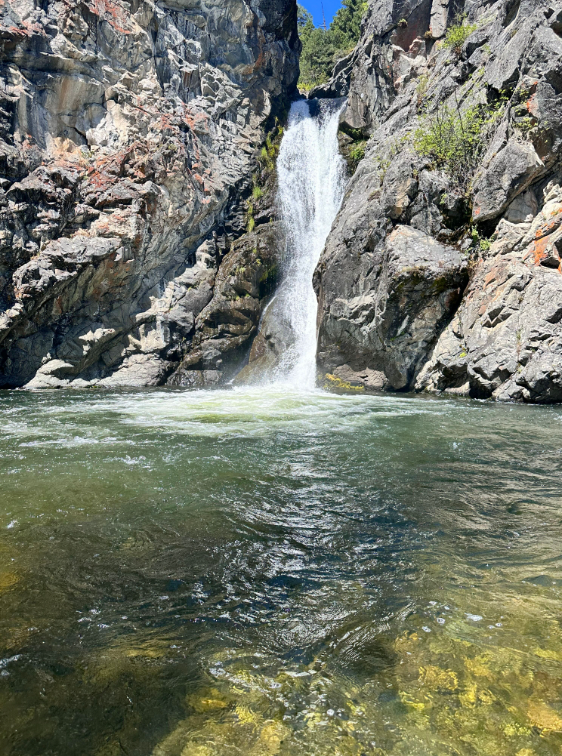 A waterfall is coming down a cliff into a river.