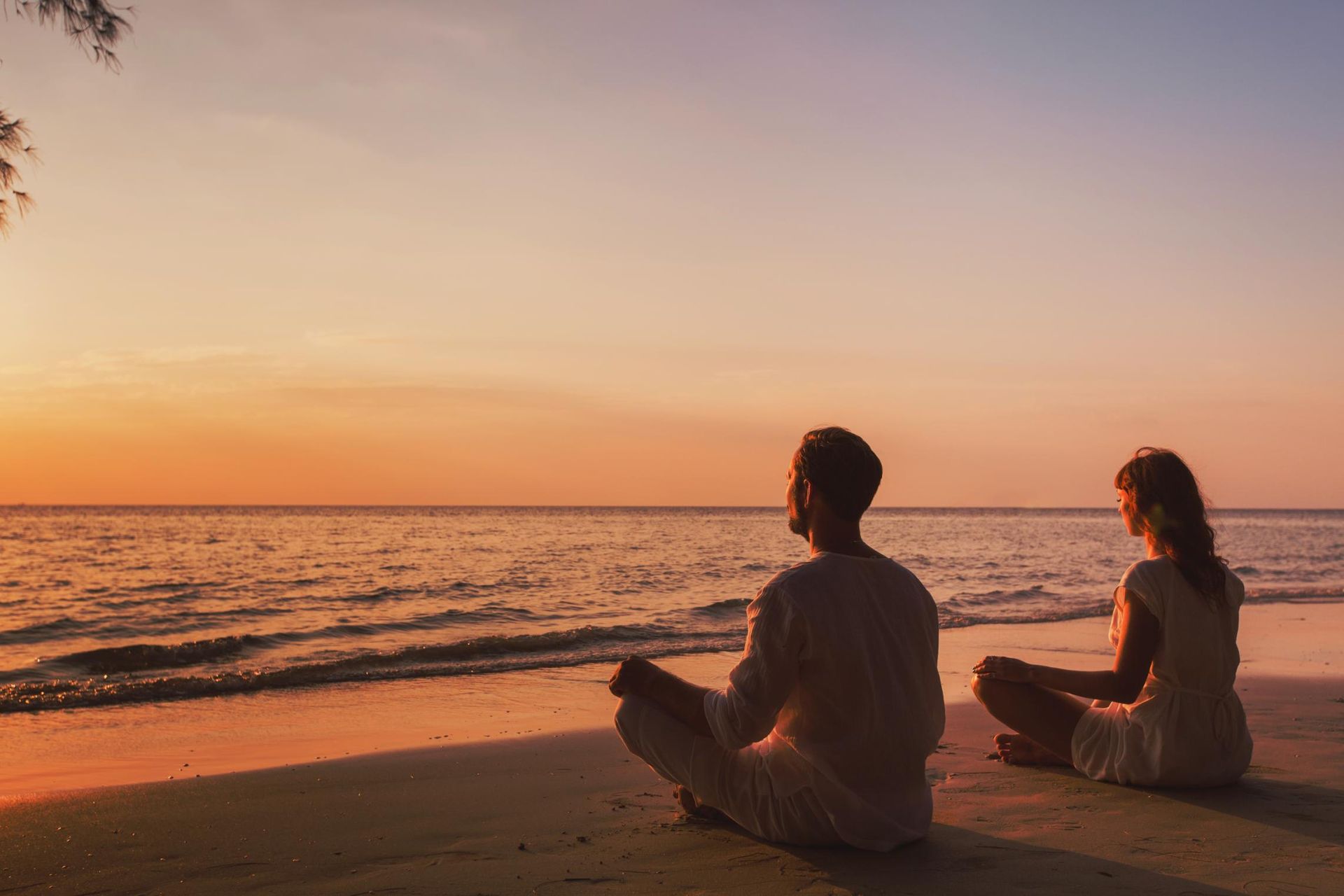 A Man And A Woman Are Sitting On The Beach At Sunset — Lake Macquarie Counselling & Psychotherapy In Cardiff, NSW