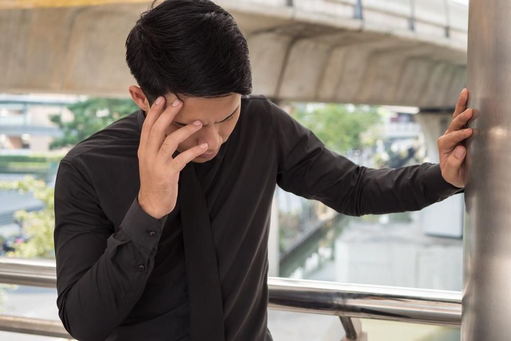 A Man Is Holding His Head While Leaning Against A Pole— Lake Macquarie Counselling & Psychotherapy In Cessnock, NSW