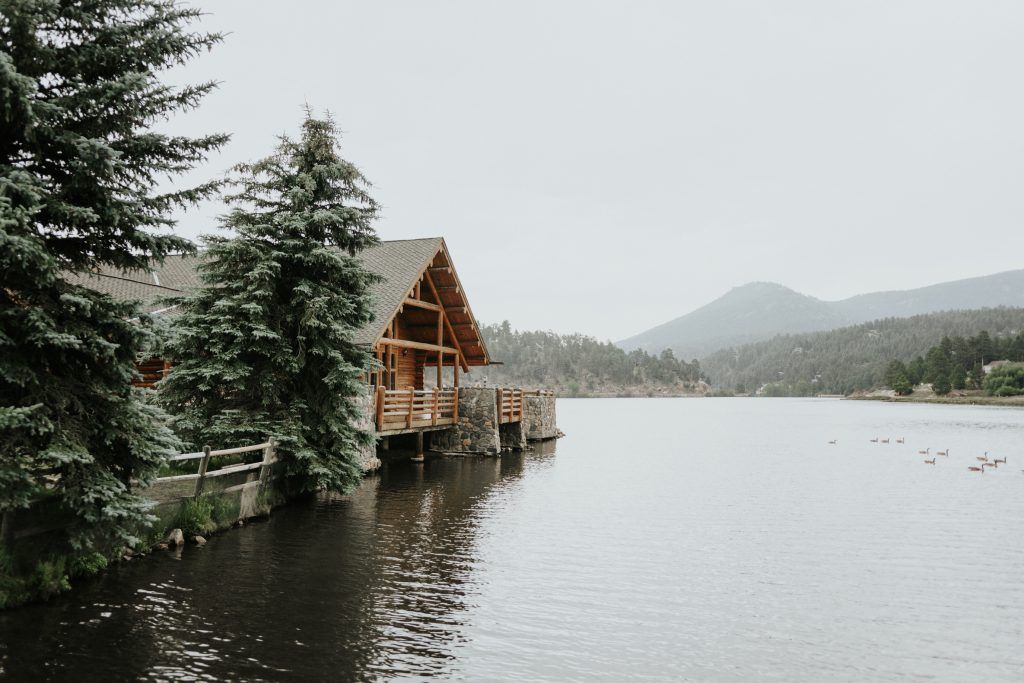 A log cabin is sitting on the shore of a lake surrounded by trees.