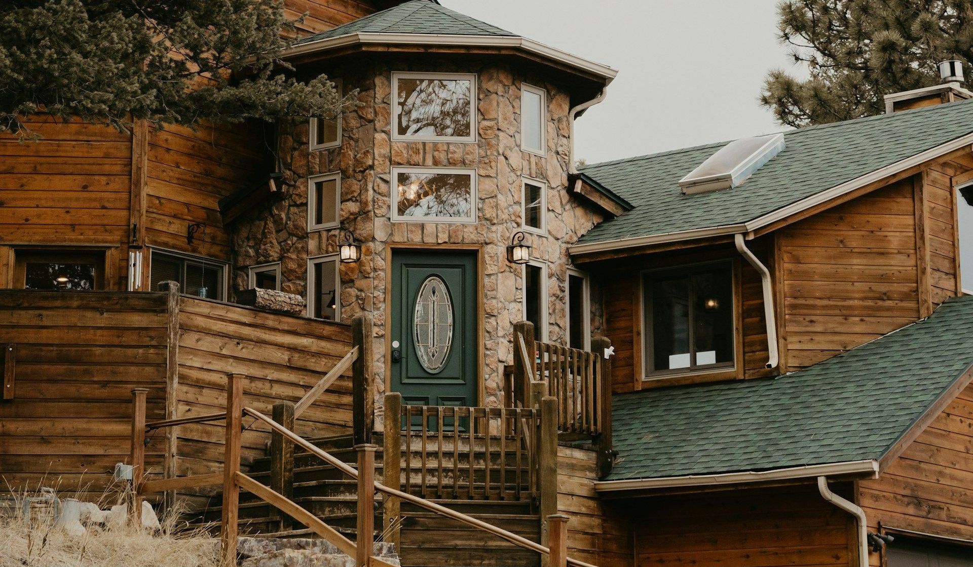 A large wooden house with a green roof and stairs leading up to it.