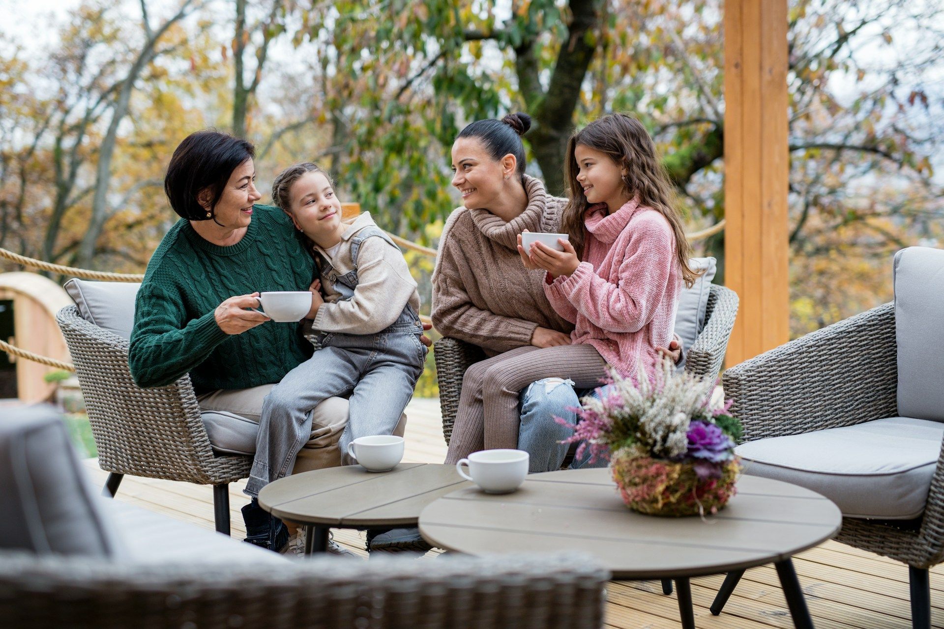 A family is sitting on a patio holding cups of coffee.