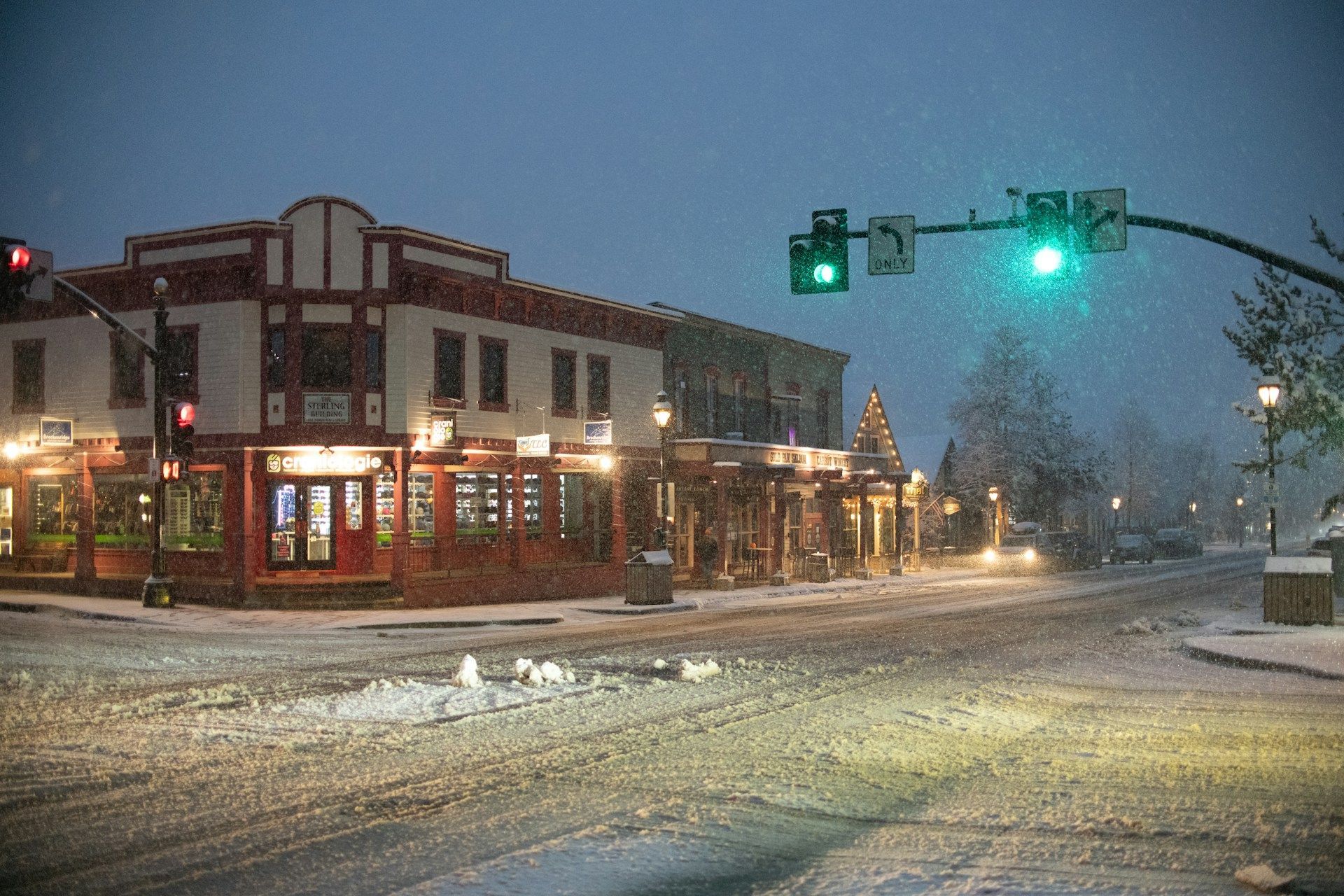 A snowy intersection with a green light and a building in the background.
